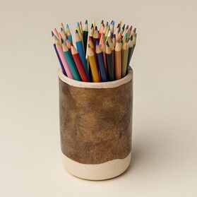 A large collection of multi-coloured pencil crayons are arranged in a gold ceramic pencil cup.